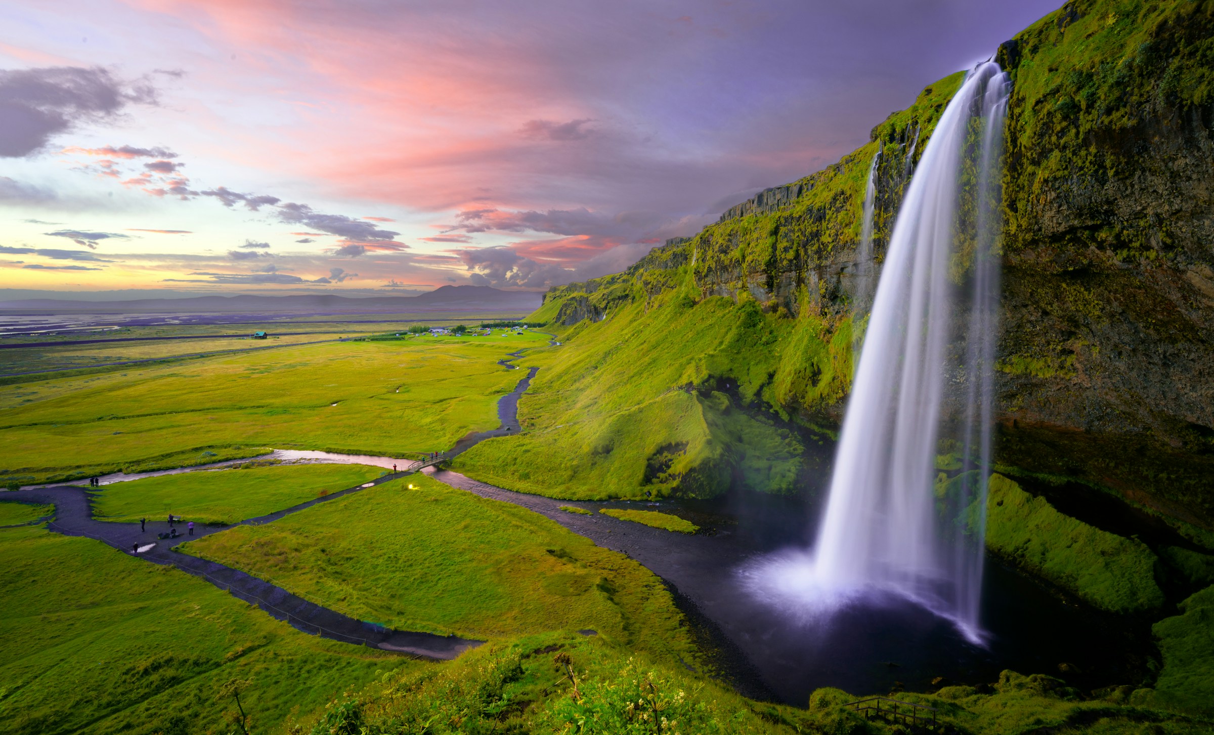 A waterfall flowing through a green Icelandic landscape